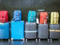 Six valises de différentes couleurs empilées, avec des sacs à dos colorés sur le dessus.