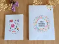 Deux carnets faits main sur fond de bois, décorés de fleurs et de points colorés.