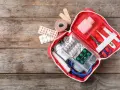 Trousse de secours pharmacie liste : pansements, rouleau de sparadrap, pilules, thermomètre, ciseaux, stéthoscope et masque.