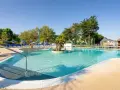 Piscine extérieure avec chaises longues bleues, parasols et végétation luxuriante sous un ciel bleu clair.