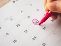 Une main entoure le 18 sur un calendrier, marquant le début des vacances scolaires à Fribourg.