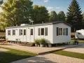 Maison mobile blanche avec terrasse en bois, table et chaises, dans un camping verdoyant.