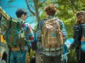 Trois jeunes avec des sacs à dos près d'un bus, prêts pour leur voyage scolaire. L'aide financière pour voyage scolaire rend ces aventures possibles.