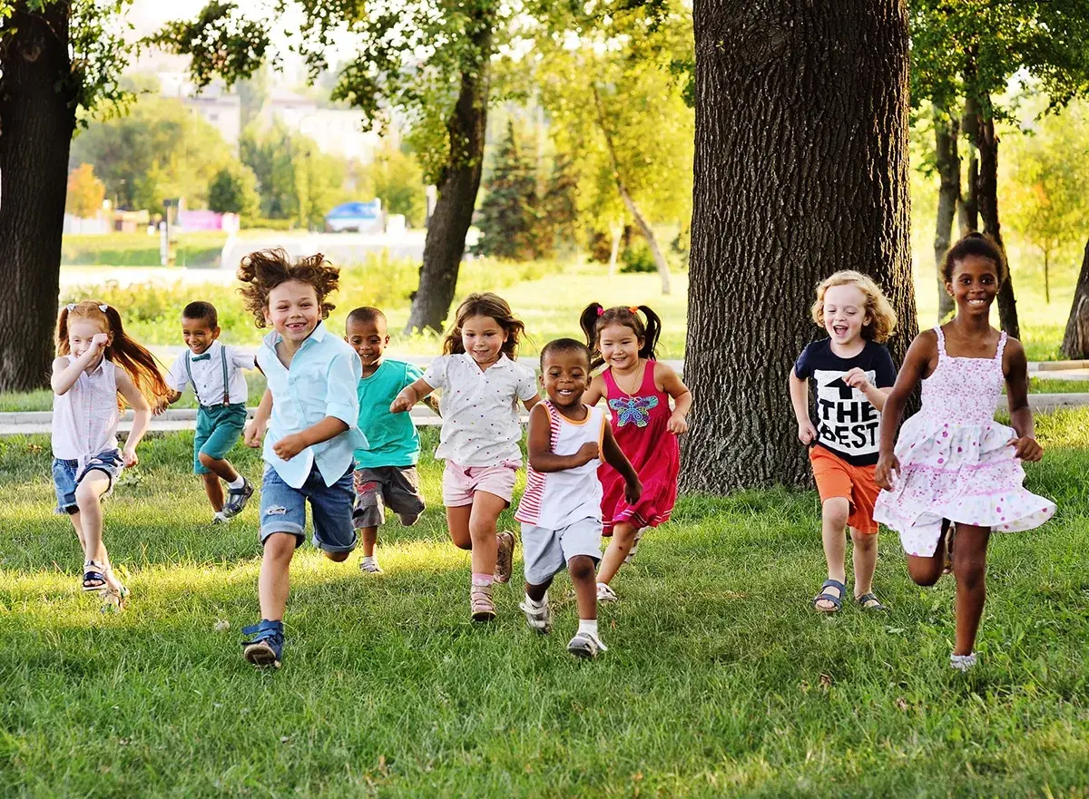 Des enfants joyeux courent dans l'herbe, profitant d'une journée ensoleillée dans une colonie de vacances 3-6 ans.