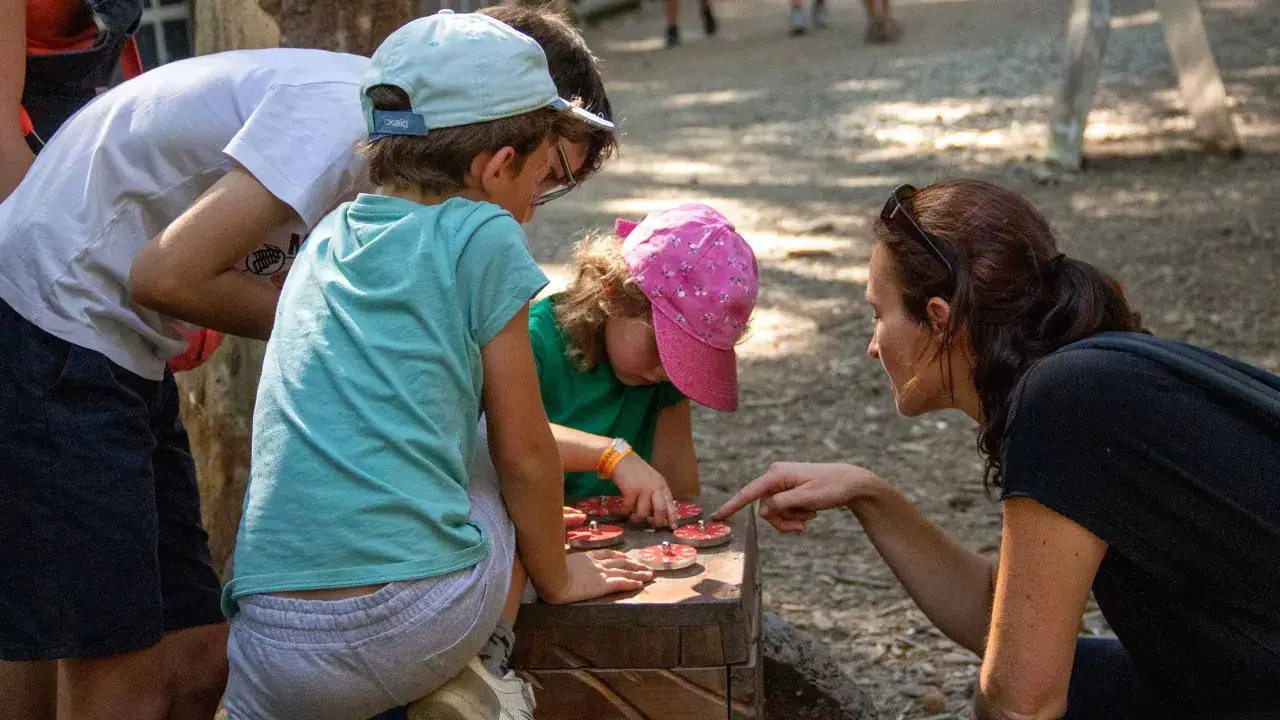 Une famille résout une énigme pour course d'orientation, manipulant des jetons sur un jeu en bois.