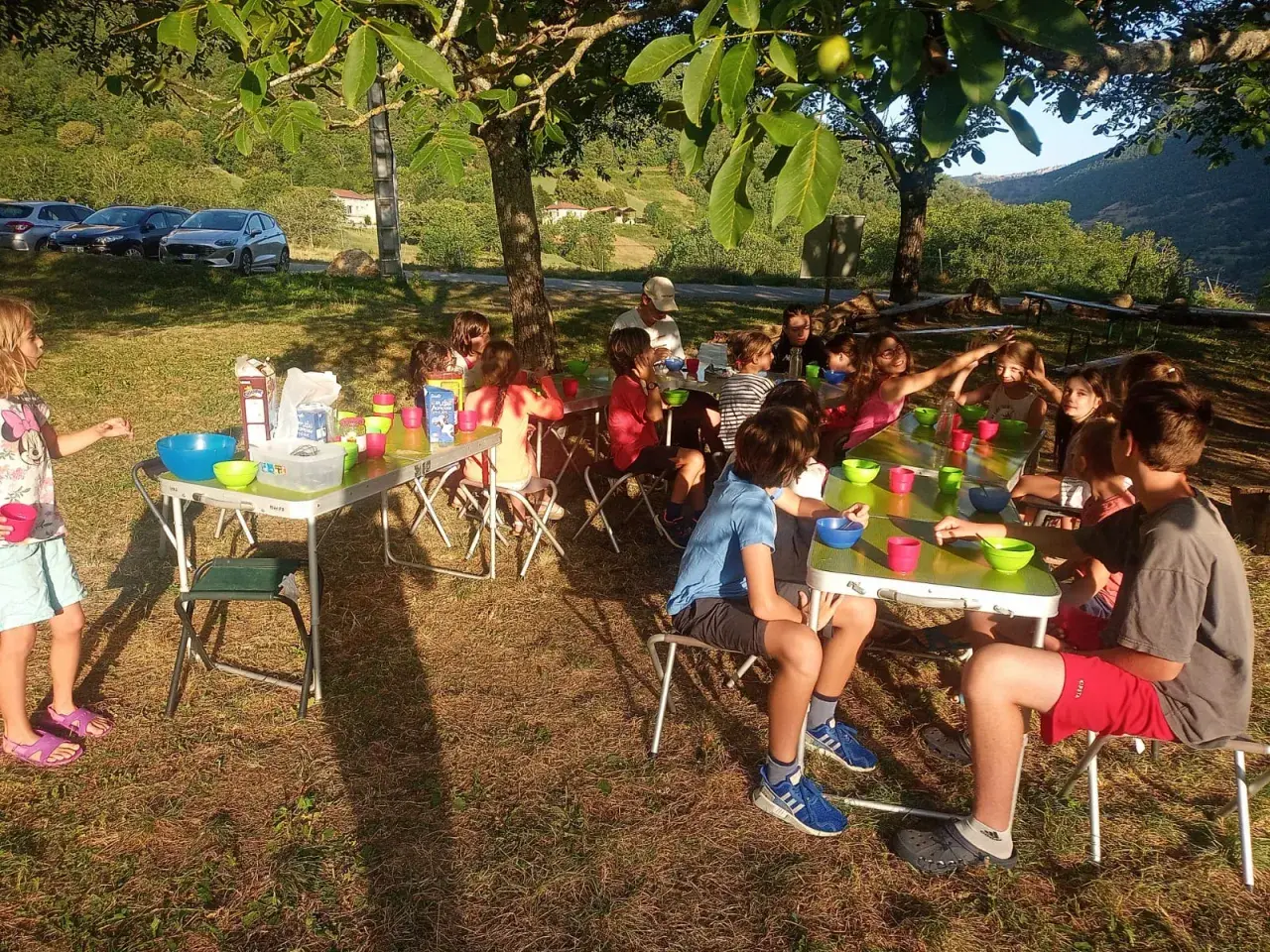 Des enfants joyeux participent à un projet d'animation en plein air, partageant un repas sous les arbres.
