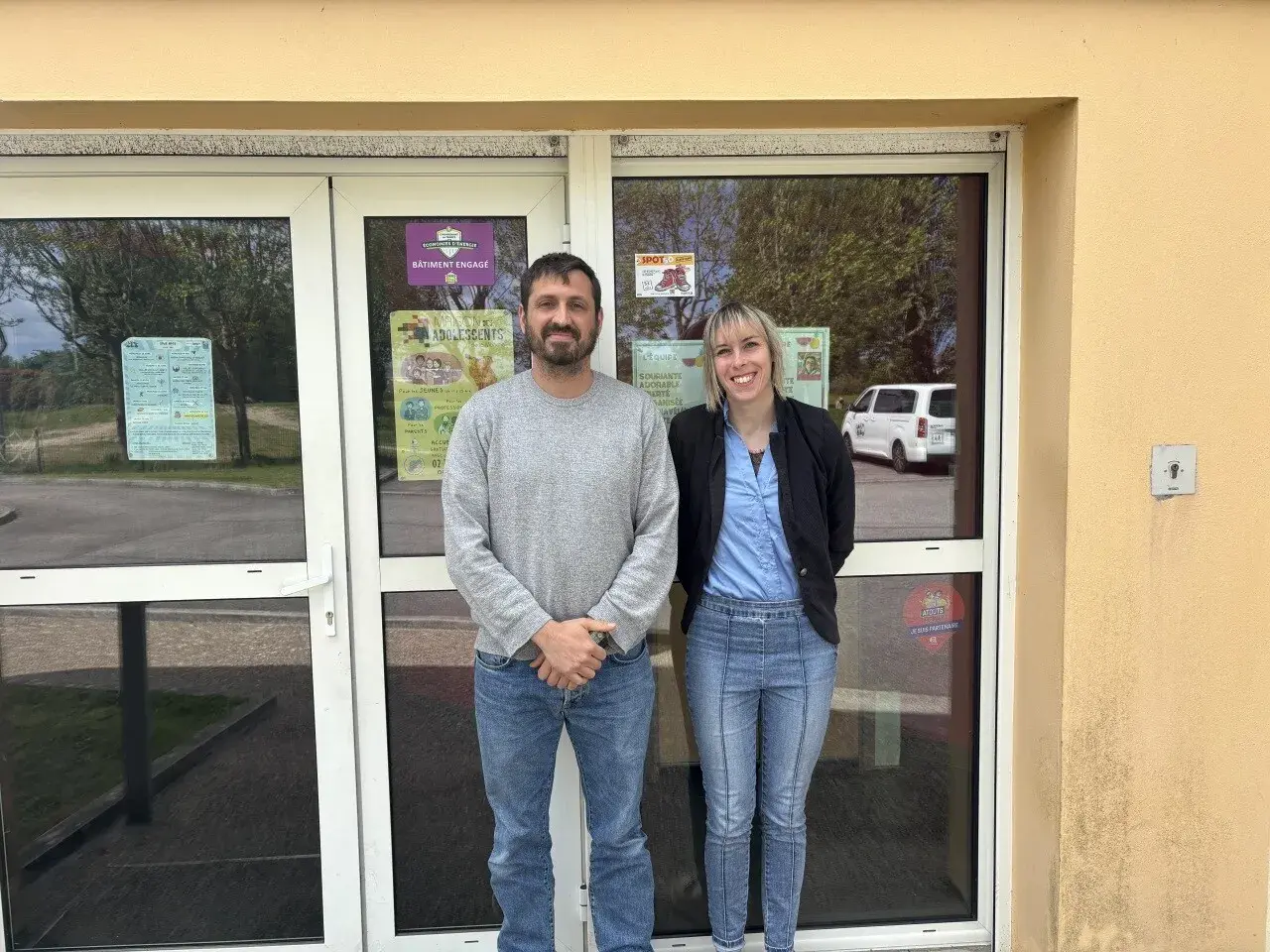 Le directeur du centre de loisirs et une collègue souriants devant l'entrée.