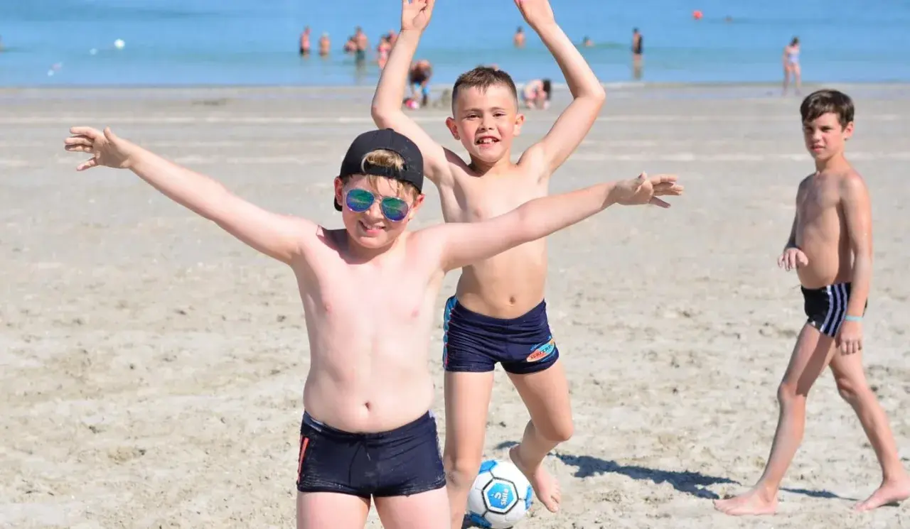 Enfants joyeux jouant au ballon sur une plage du colo sud de la France.