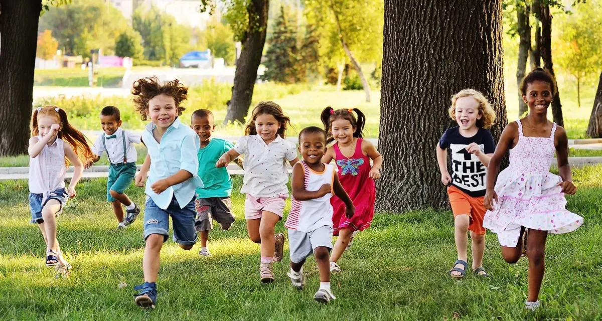 Des enfants joyeux courent dans l'herbe, profitant d'une journée ensoleillée dans une colonie de vacances 3-6 ans.