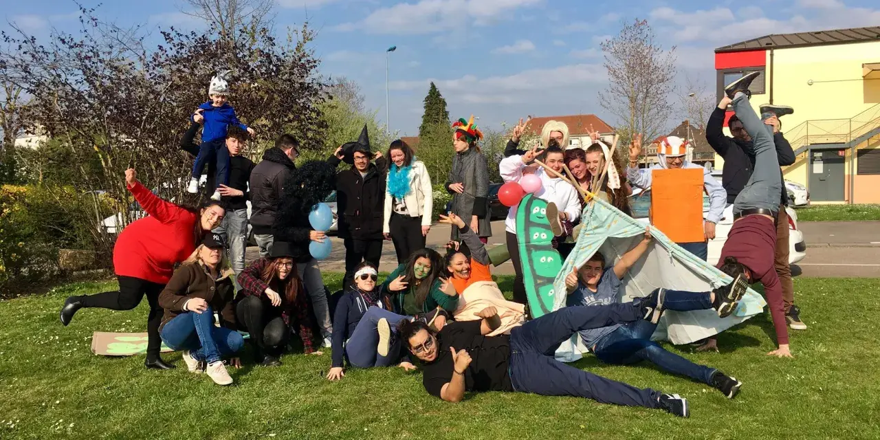 Groupe de jeunes en costumes et déguisements, certains sur une tente, sur l'herbe par beau temps.