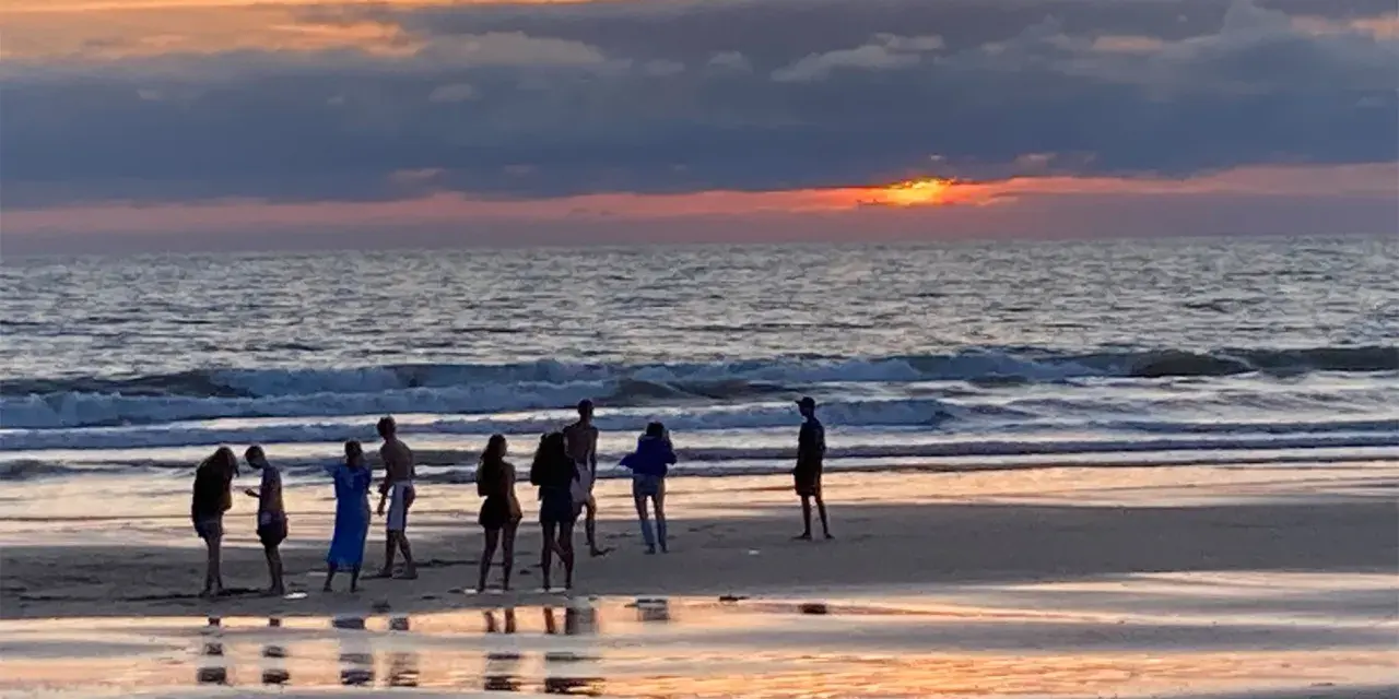 Coucher de soleil sur une plage avec des silhouettes de personnes.