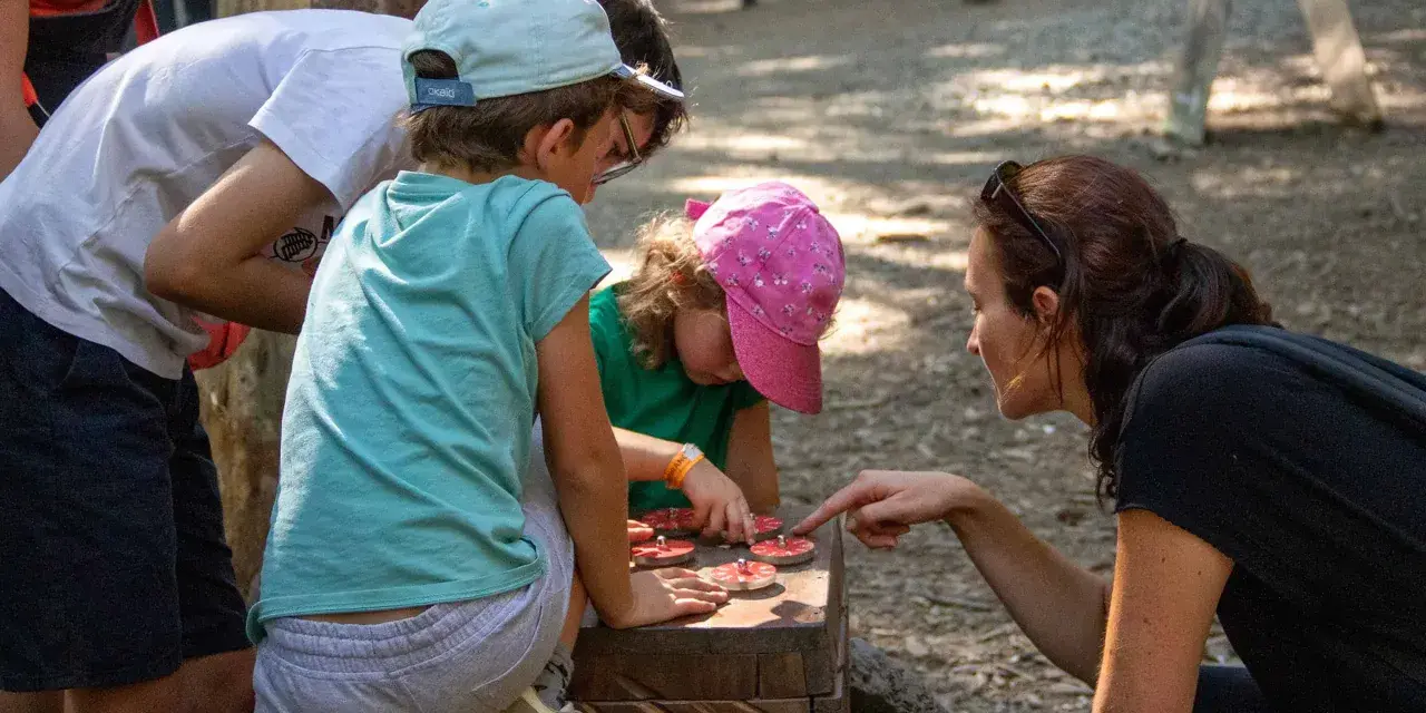 Une famille résout une énigme pour course d'orientation, manipulant des jetons sur un jeu en bois.