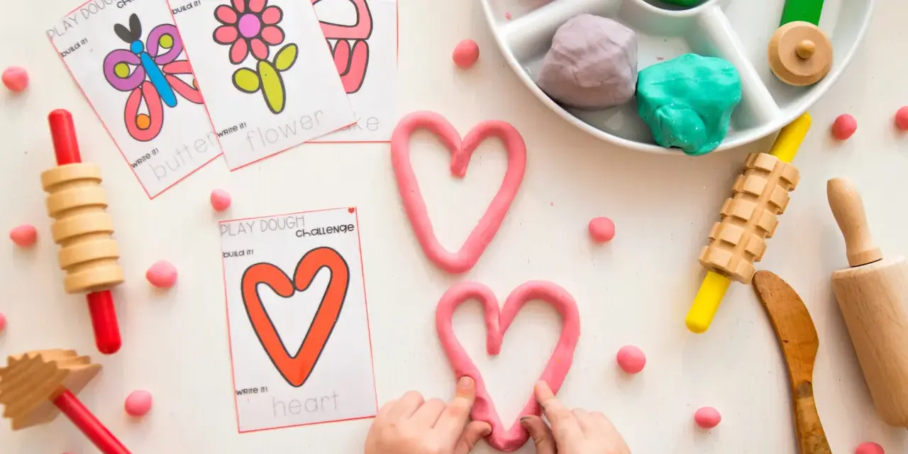 Pâte à modeler rose en forme de cœur, cartes d'activités, rouleaux et petites boules de pâte.