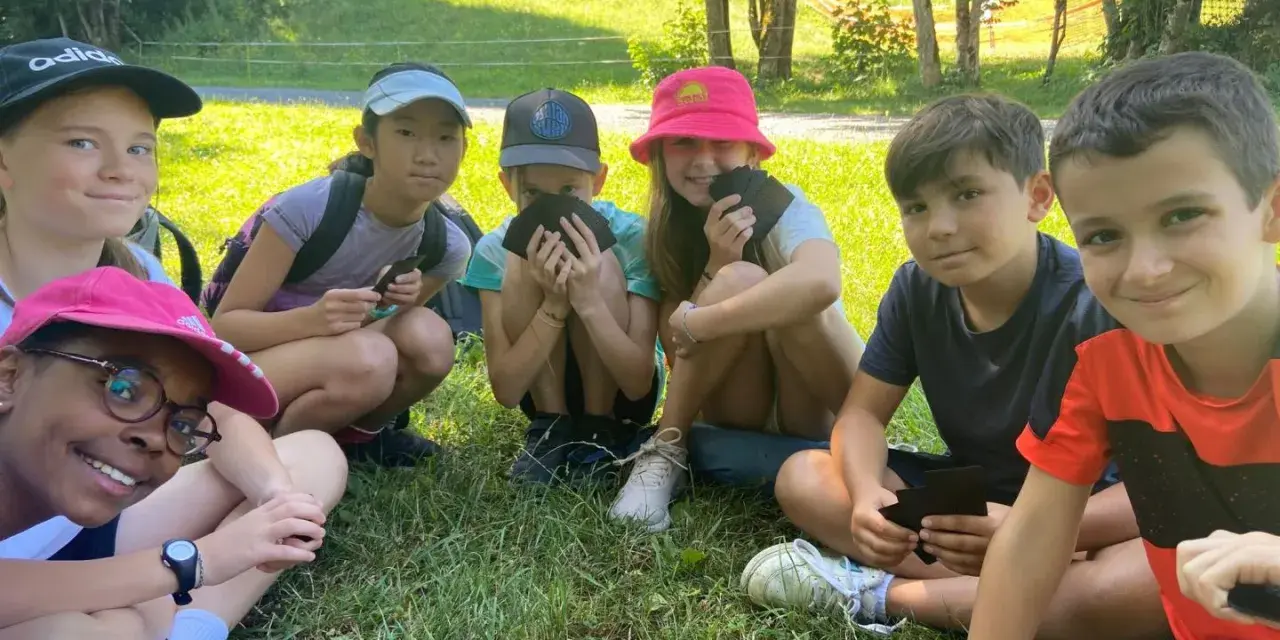Groupe d'enfants souriants assis dans l'herbe, certains tenant des cartes.