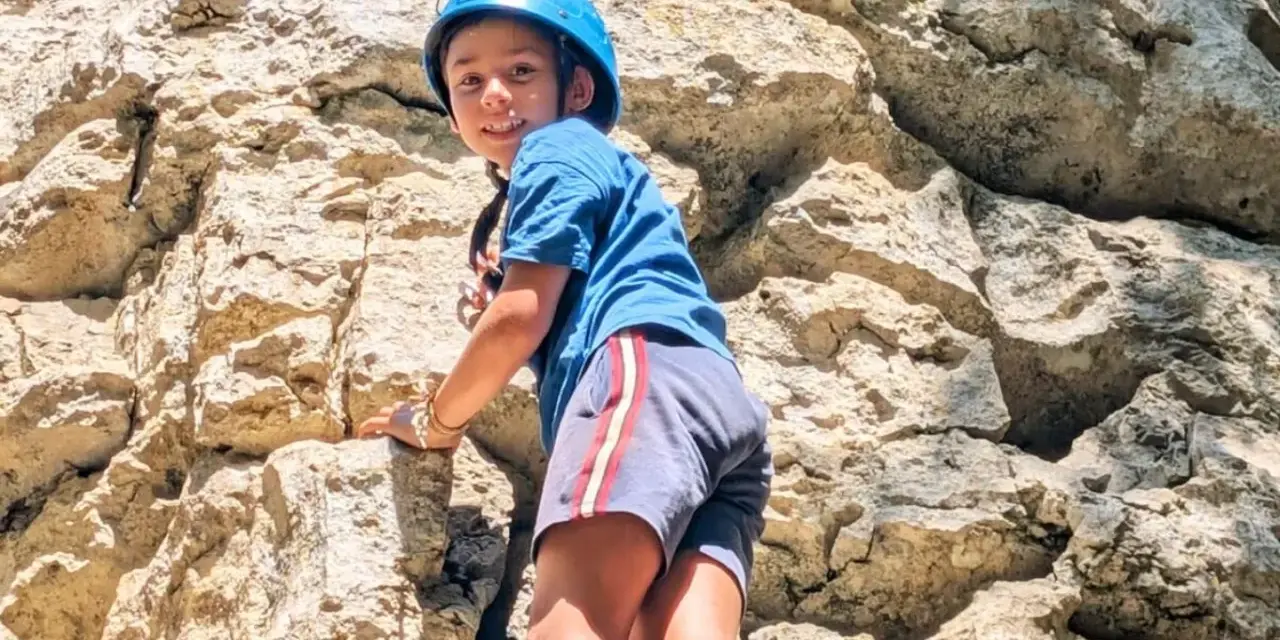 Enfant souriant escaladant un rocher avec un casque bleu.
