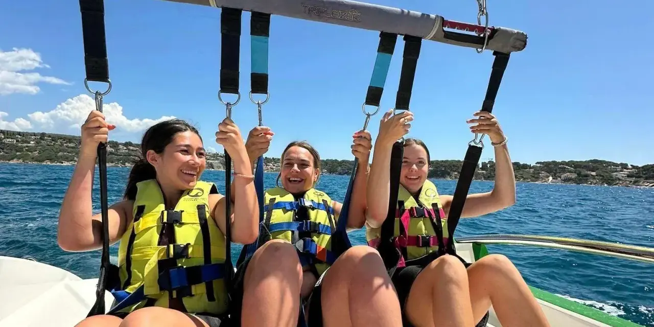 Trois jeunes femmes souriantes en parachute ascensionnel au-dessus de la mer.
