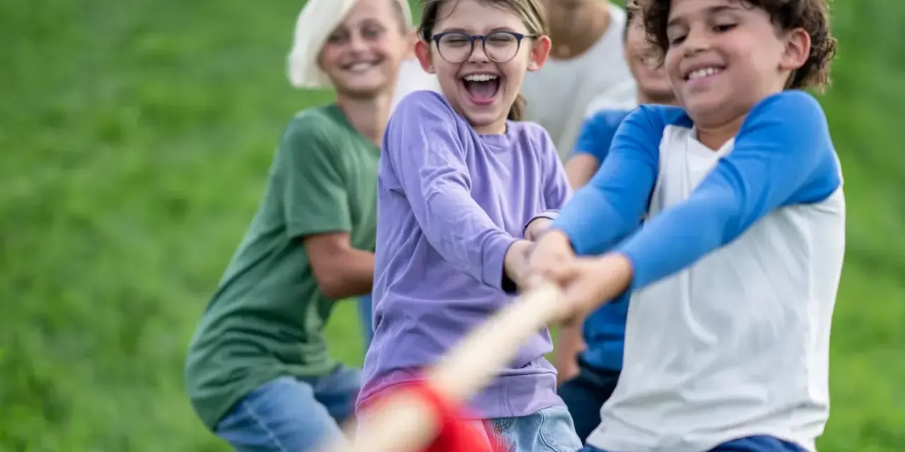 Des enfants joyeux jouent à la corde dans un champ d'herbe verte.