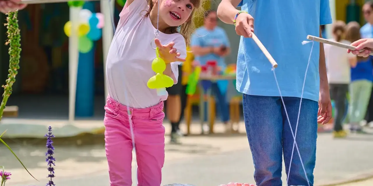 Une petite fille joyeuse participe à des jeux de kermesse pour tout petit, essayant d'attraper un jouet jaune avec une canne à pêche improvisée.