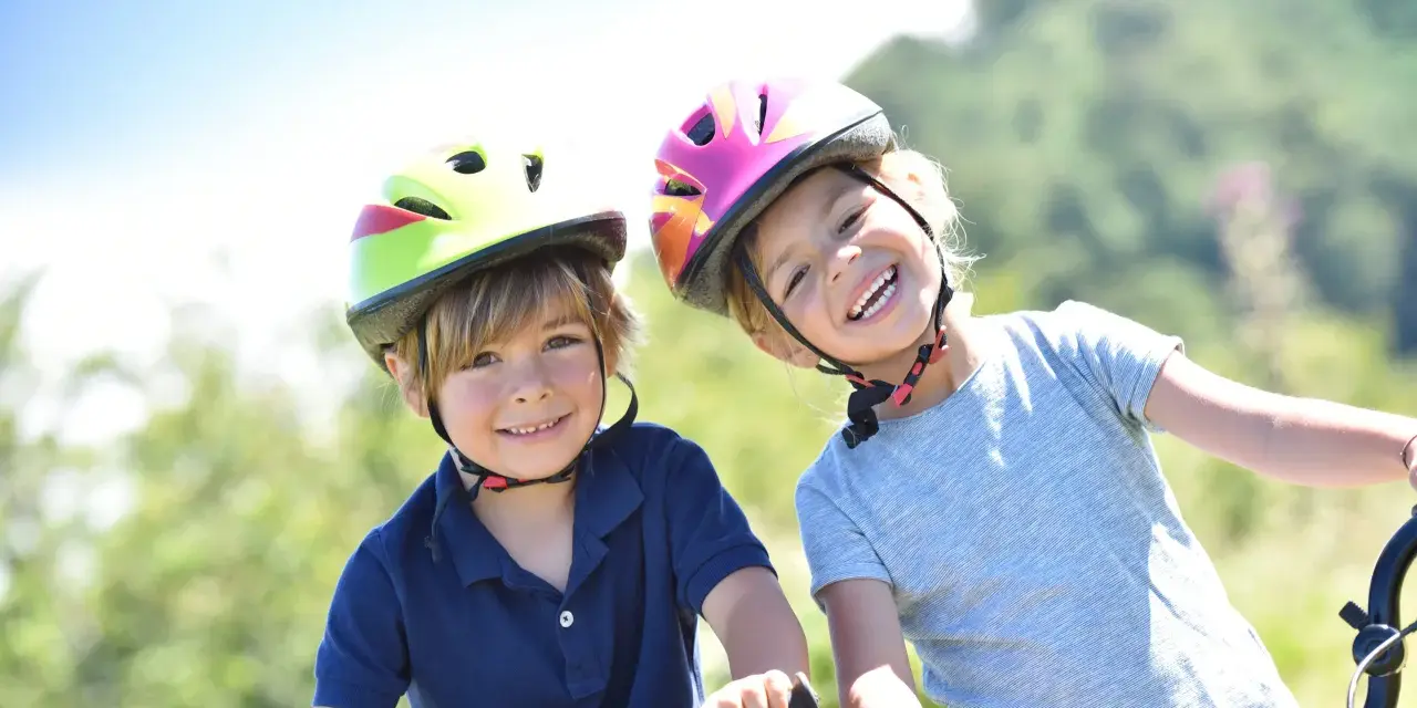 Deux enfants souriants, casques de vélo colorés, profitent de leurs vacances scolaires en Savoie.