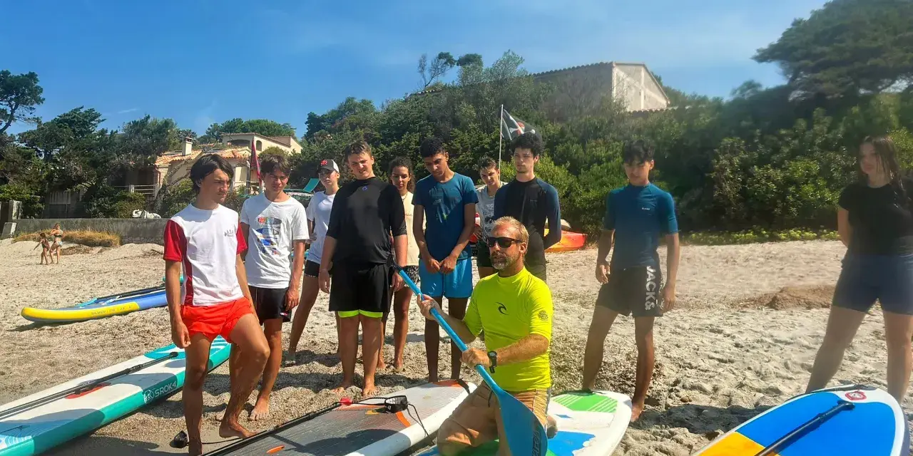 Un groupe d'adolescents et un moniteur sur une plage avec des planches de paddle.