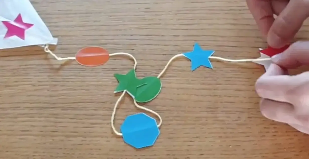 Fabrication d'un cerf-volant étoile : fils, formes colorées (étoiles, ovales, octogone) et mains.