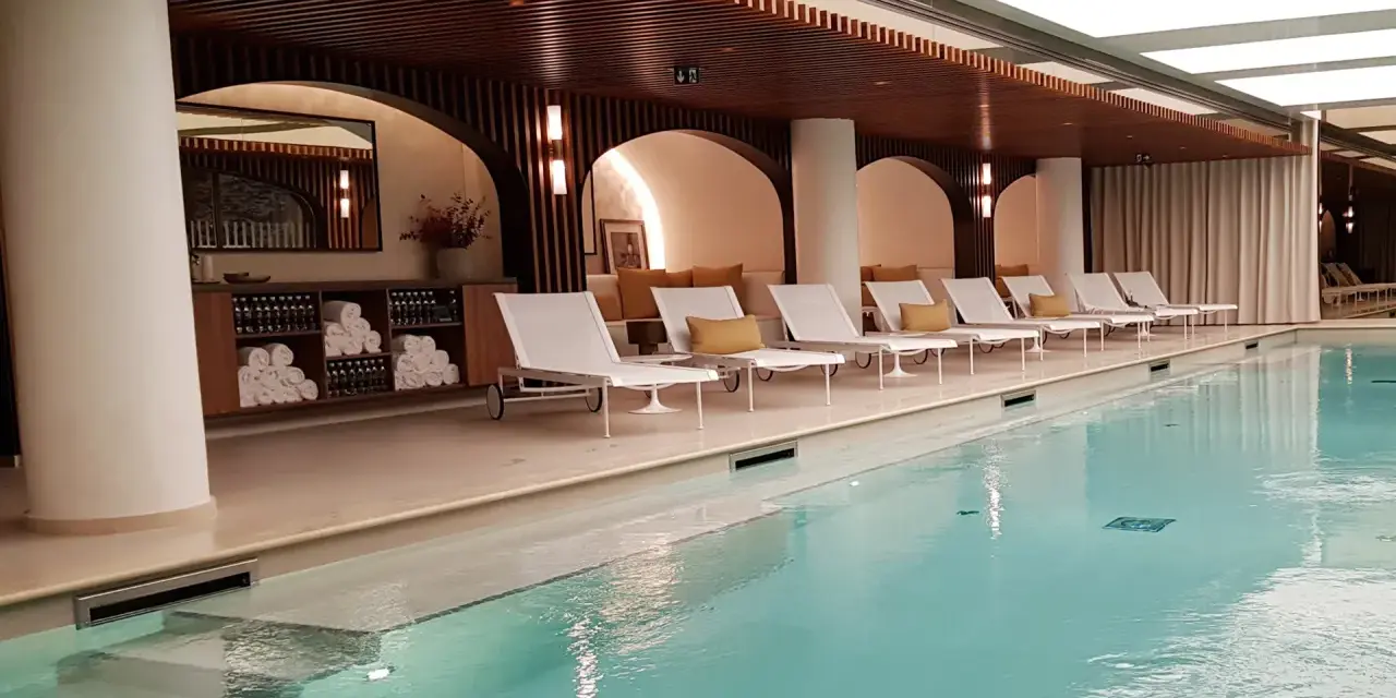 Piscine intérieure avec chaises longues blanches, coussins jaunes et étagères de serviettes.