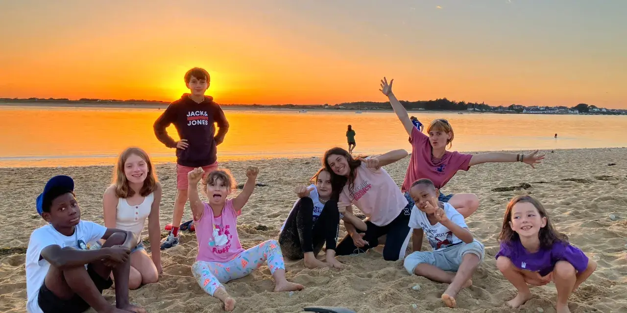 Groupe d'enfants joyeux sur une plage au coucher du soleil.