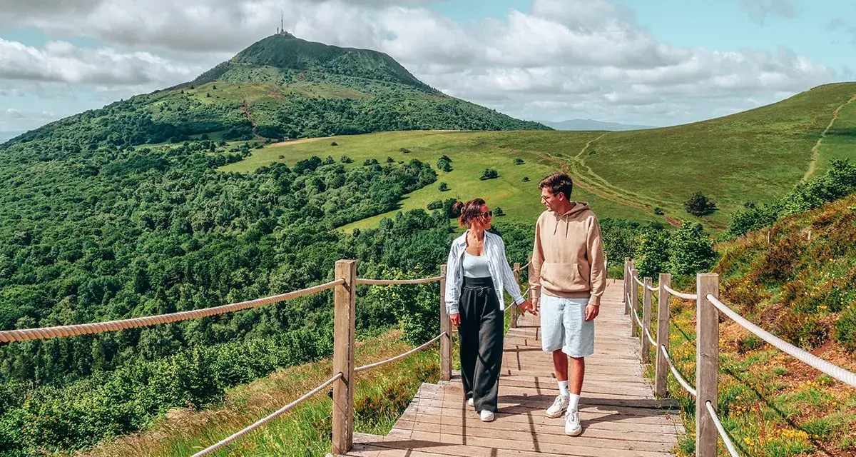 Couple marchant sur un chemin en bois avec un volcan en arrière-plan en Auvergne.