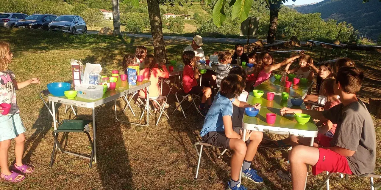 Des enfants joyeux participent à un projet d'animation en plein air, partageant un repas sous les arbres.