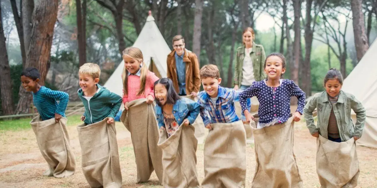 Des enfants participent à une course en sac dans un camp de vacances en forêt.