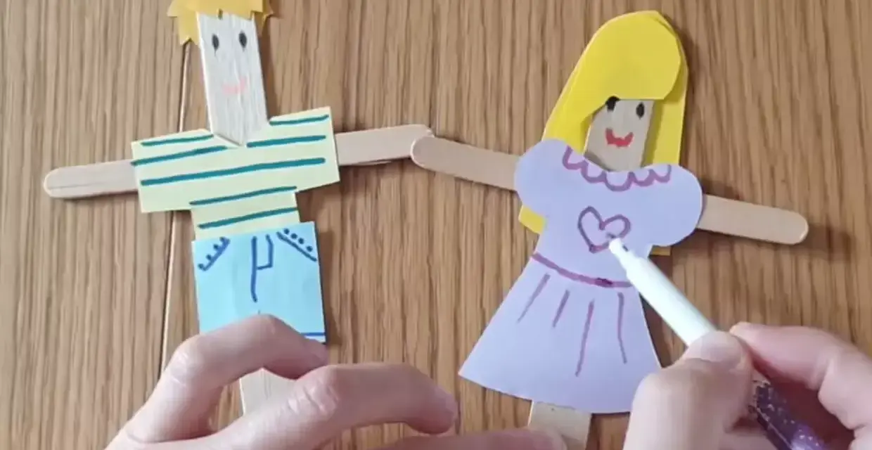 Poupées en bâtonnets de bois, une fille et un garçon, décorées par des mains d'enfant.