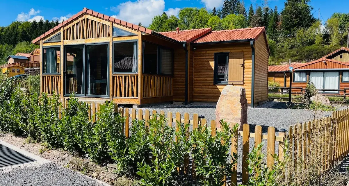 Chalets en bois avec clôture et végétation devant, sous un ciel bleu.