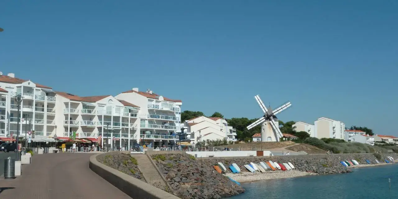 Vue de Jard-sur-Mer avec son port, ses immeubles blancs, son moulin et sa plage bordée de bateaux.