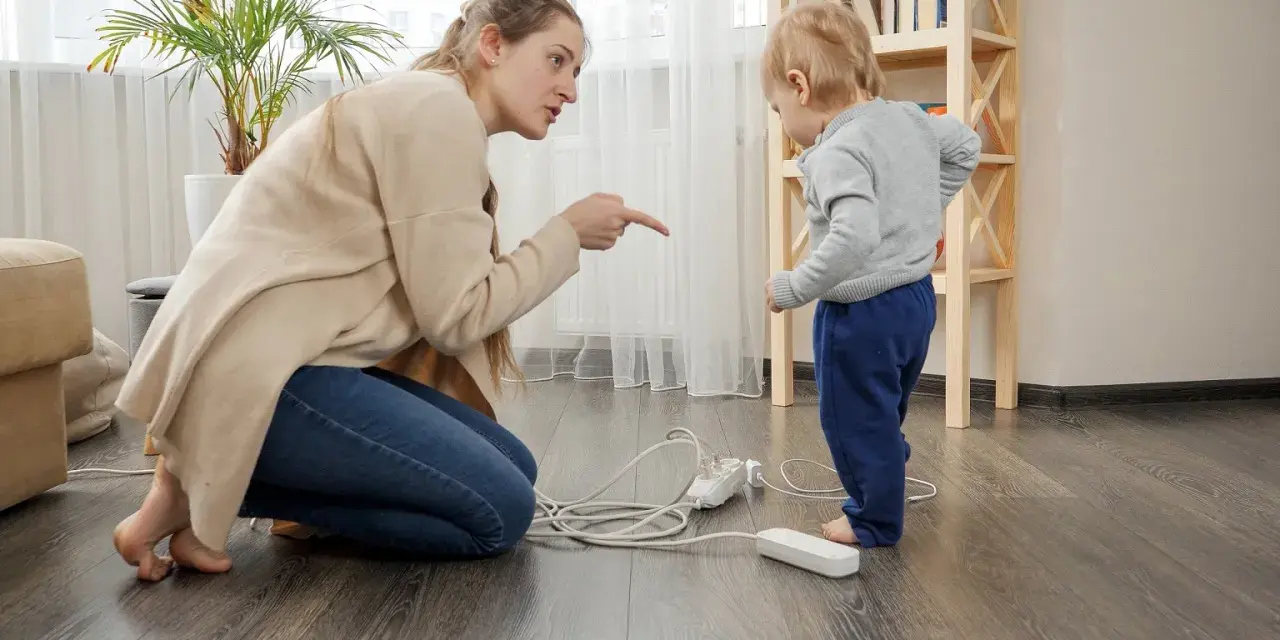 Une femme réprimande un enfant près de prises électriques au sol.