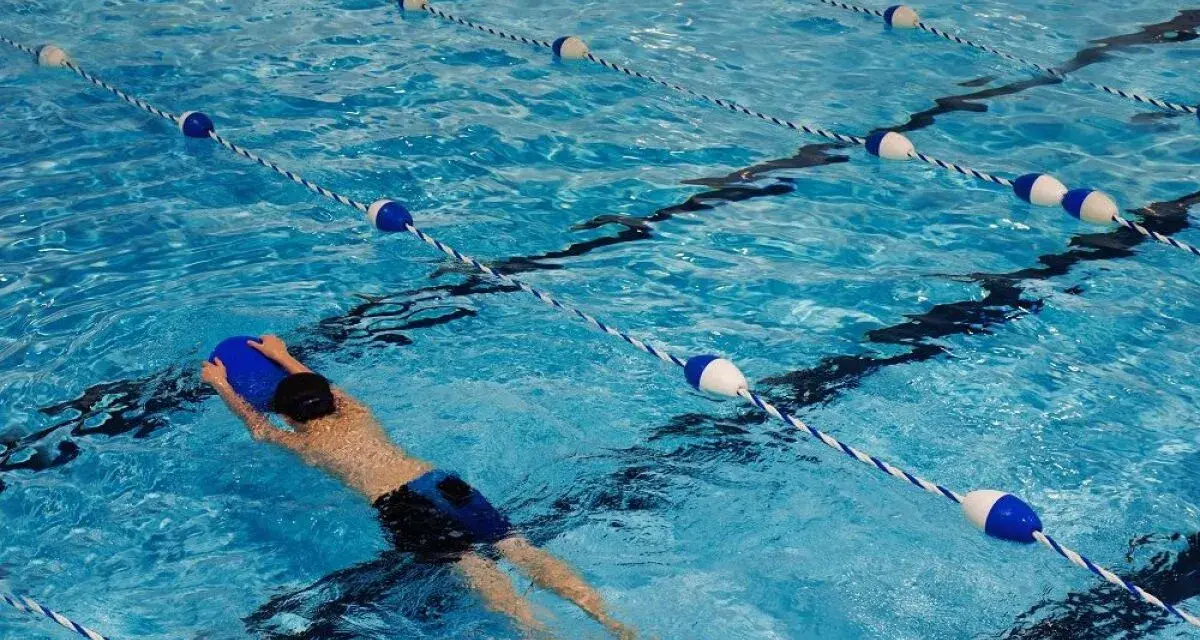 Un nageur utilise une planche bleue dans une piscine avec des lignes de bouées bleues et blanches.