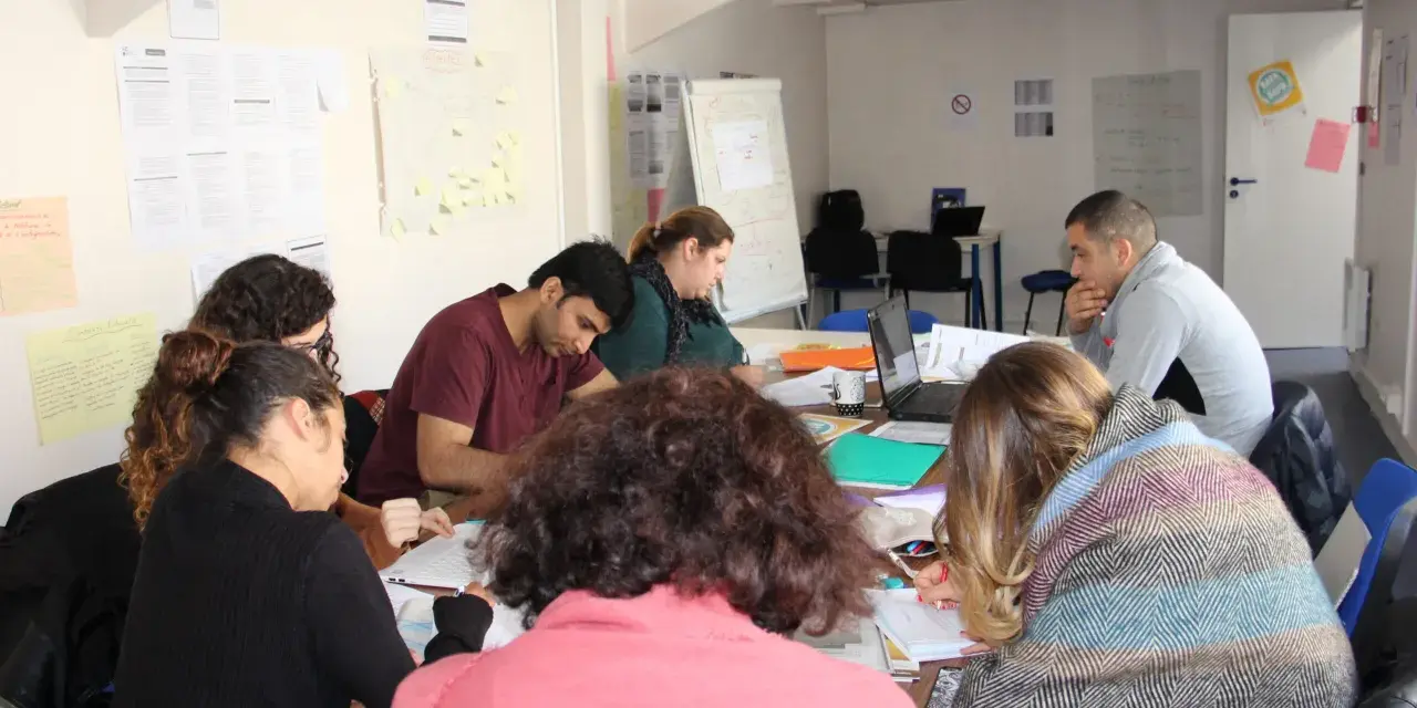 Groupe de personnes assises autour d'une table, travaillant sur des documents et un ordinateur portable.