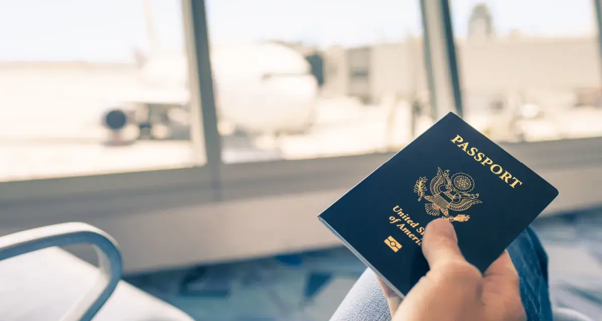 Main tenant une carte d'identité américaine devant une fenêtre d'aéroport avec un avion en arrière-plan.