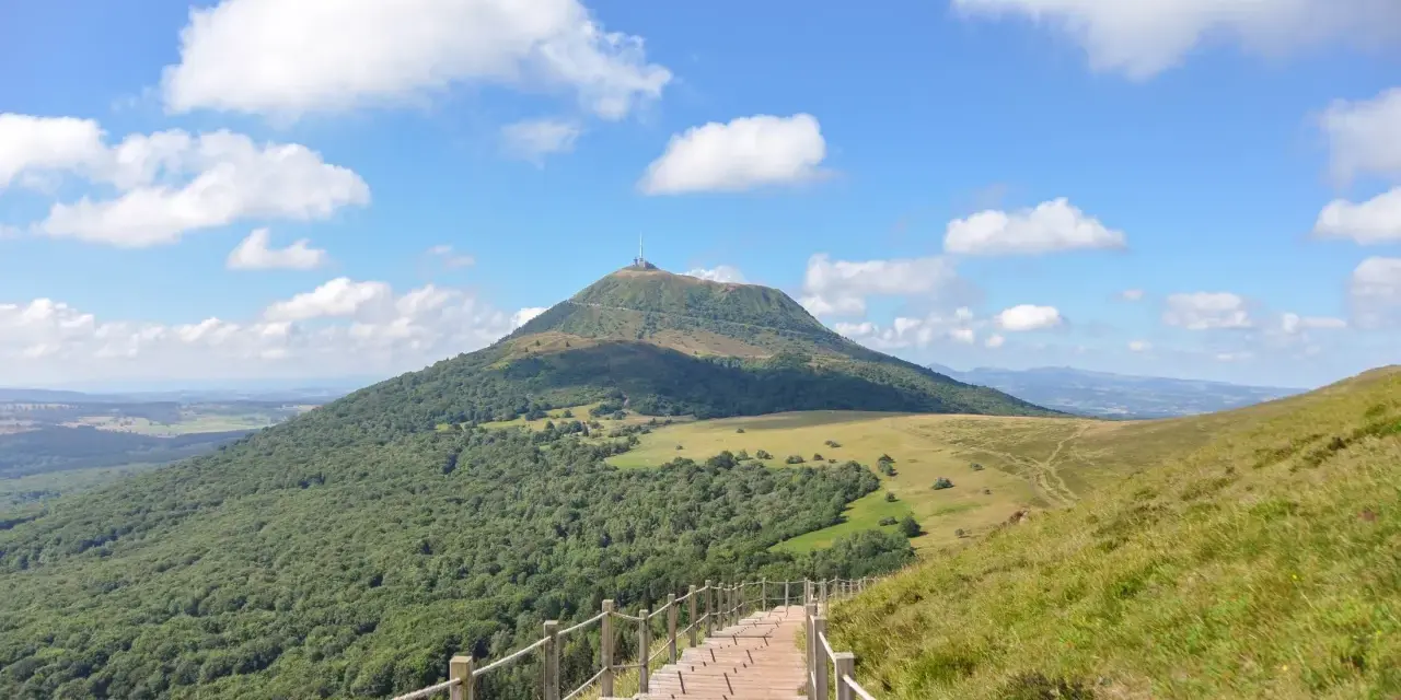 Escalier en bois menant au Puy de Dôme sous un ciel bleu et nuageux.