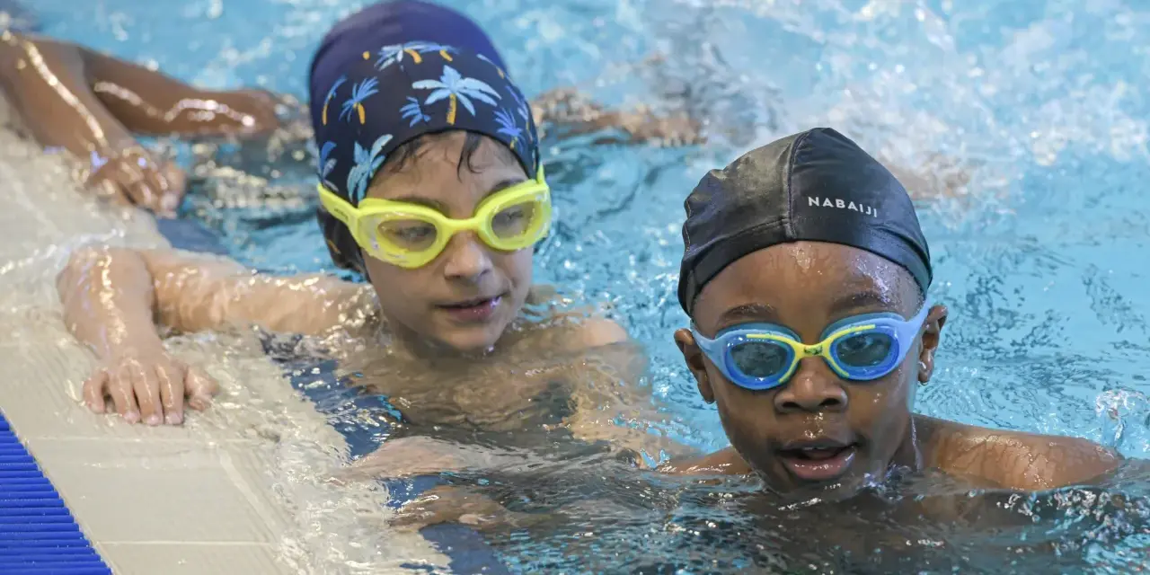 Deux enfants avec des bonnets et lunettes de natation dans une piscine.
