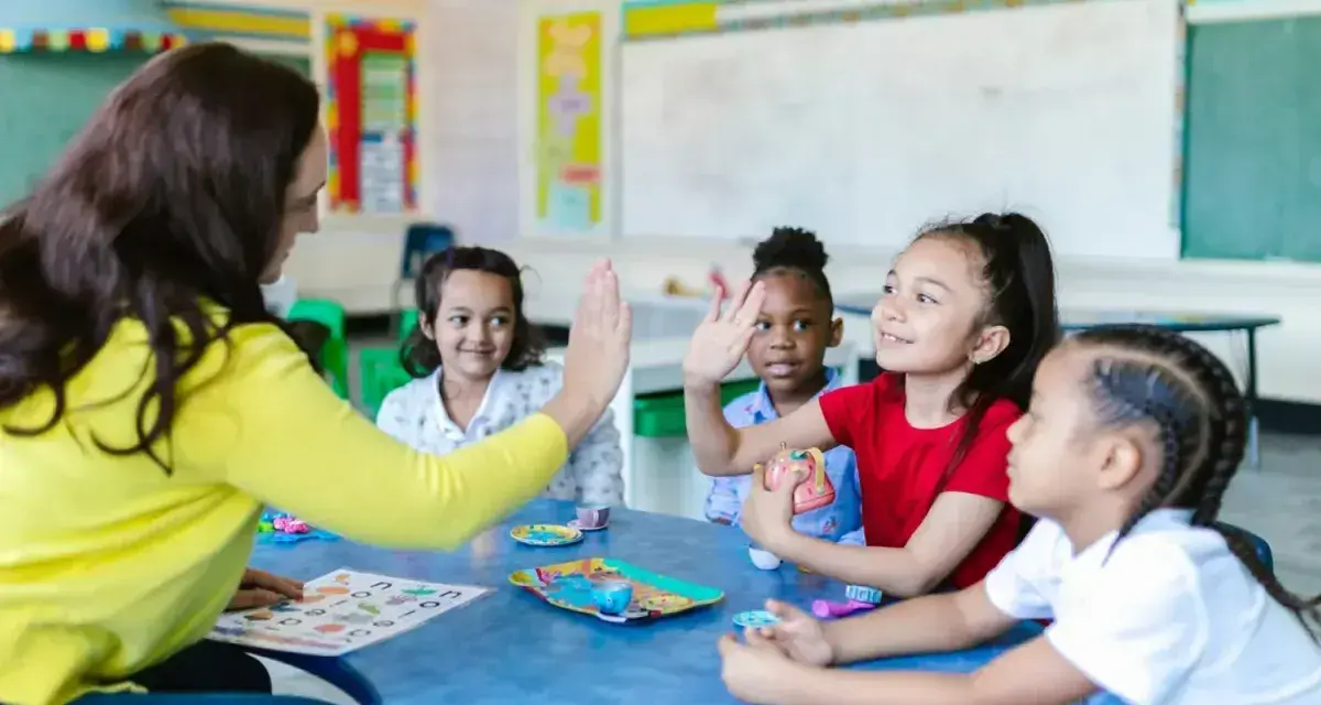 Une enseignante donne une tape dans la main à des enfants autour d'une table dans une salle de classe.