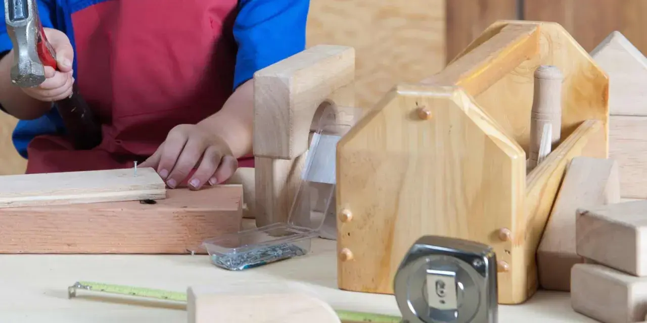 Enfant bricolant avec un marteau, des clous, un mètre ruban et des outils en bois.