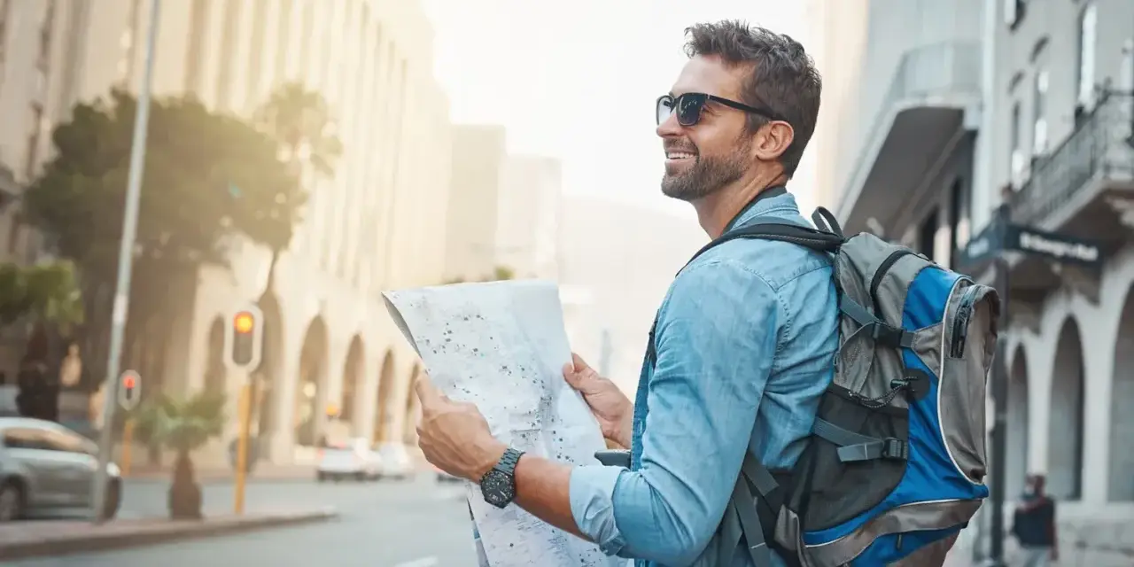 Un homme souriant avec un sac à dos consulte une carte, prêt pour un voyage en immersion dans la ville.