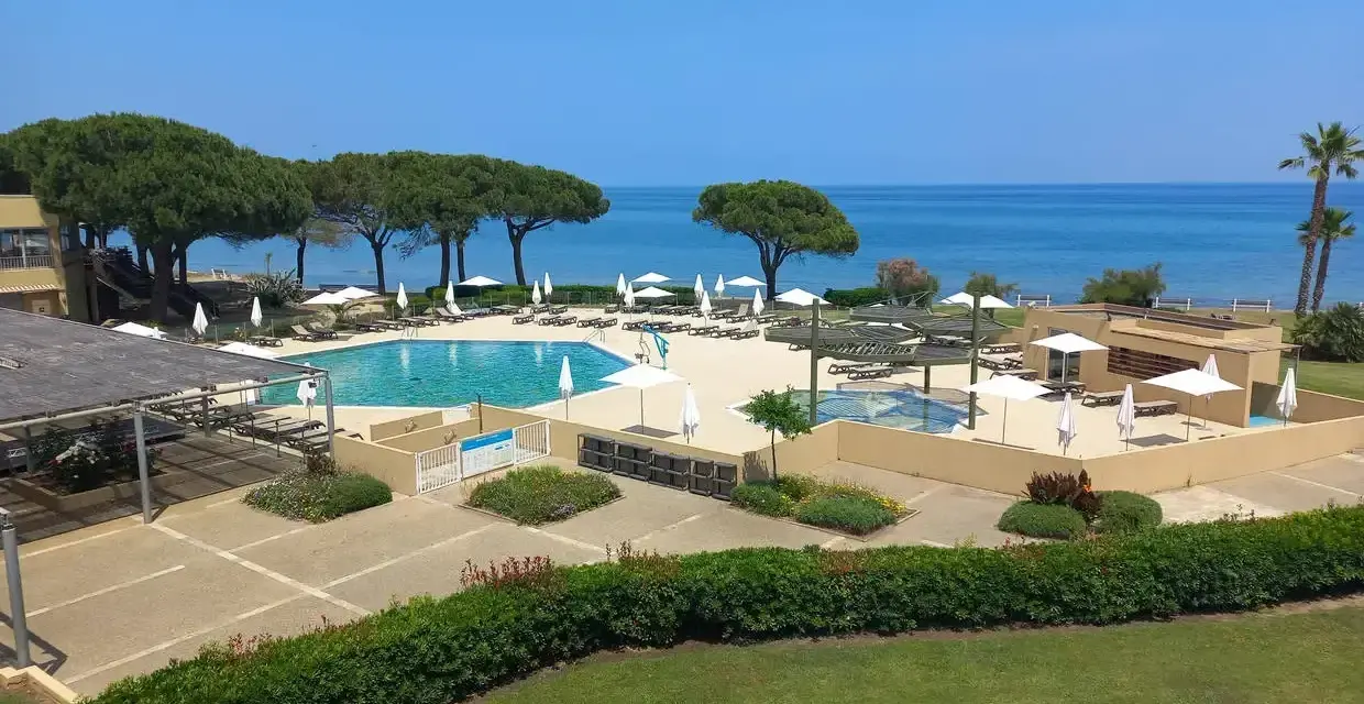 Piscine et transats dans un complexe hôtelier en bord de mer, sous un ciel bleu.