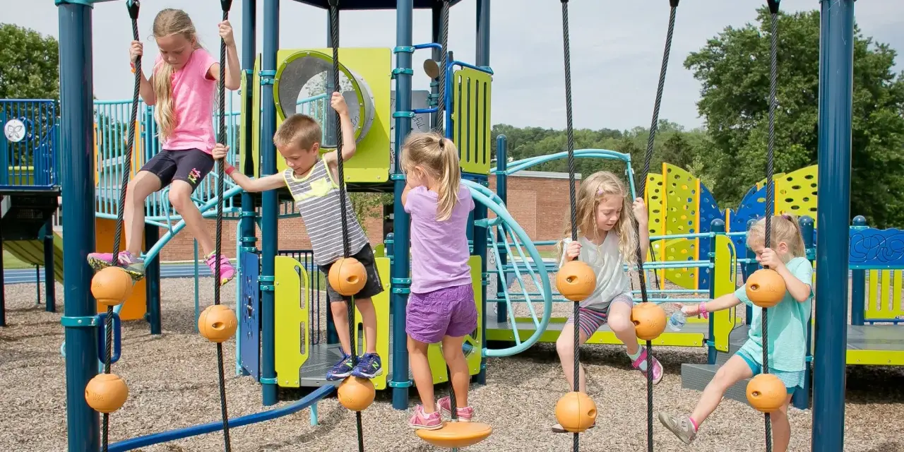 Enfants jouant sur une structure d'escalade avec des cordes et des balles oranges.