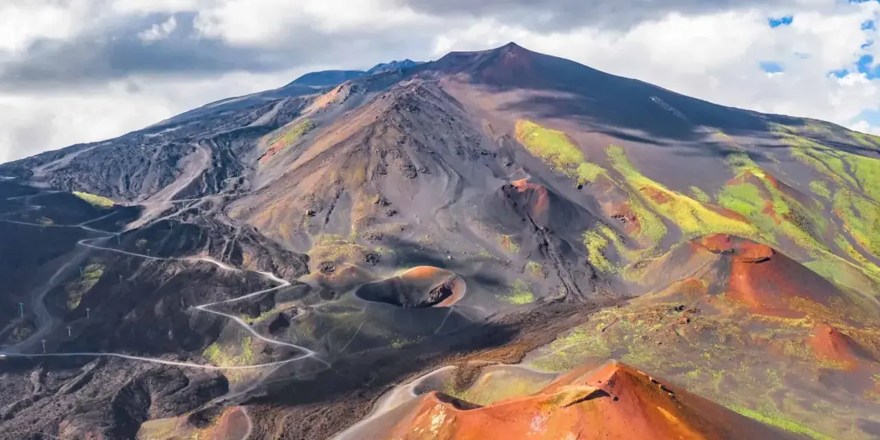 Vue aérienne de l'Etna, avec ses cratères rouges et ses pentes noires et vertes.