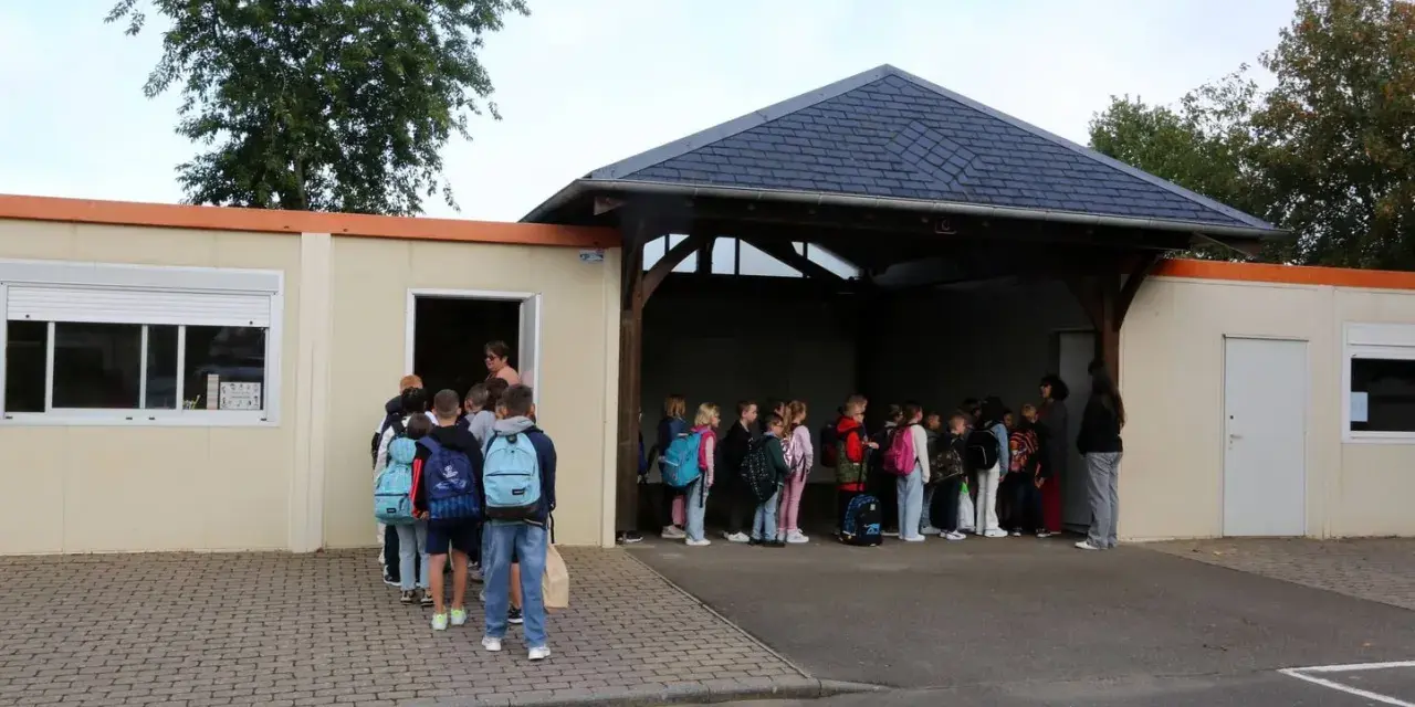 Des enfants font la queue devant un bâtiment scolaire, certains avec des sacs à dos.