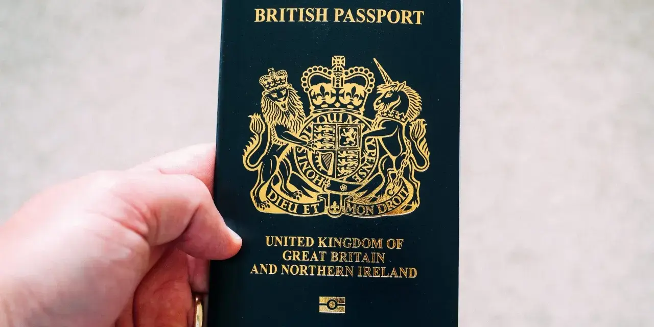 Main d'une personne tenant un passeport britannique bleu foncé avec le blason royal doré.