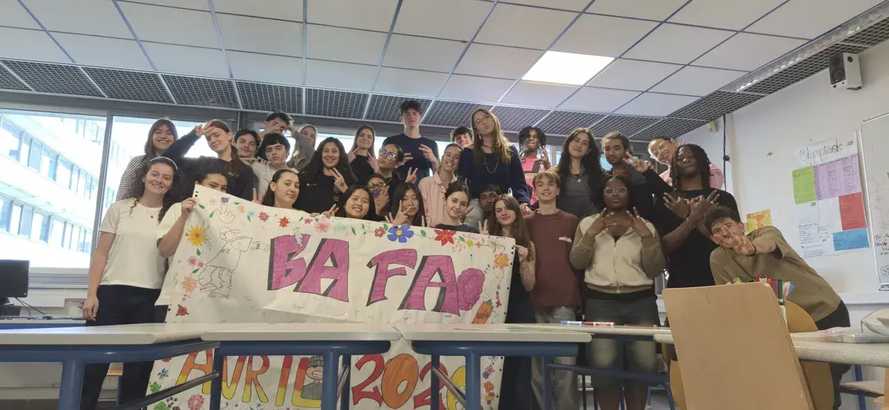 Un groupe d'étudiants pose derrière une banderole "BAFA" décorée de dessins et de fleurs.