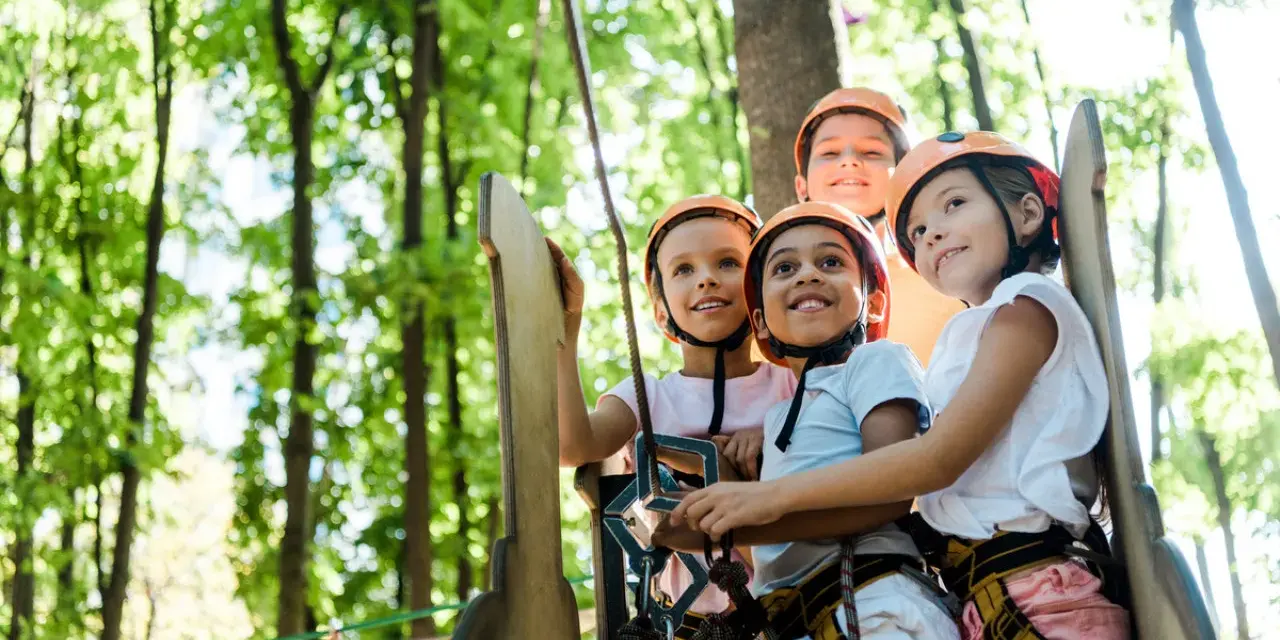 Quatre enfants souriants portant des casques de sécurité dans un parc d'aventure.