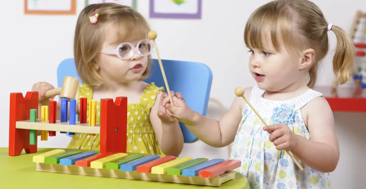 Deux petites filles s'amusent avec un xylophone, explorant la musique et les activités manuelles.
